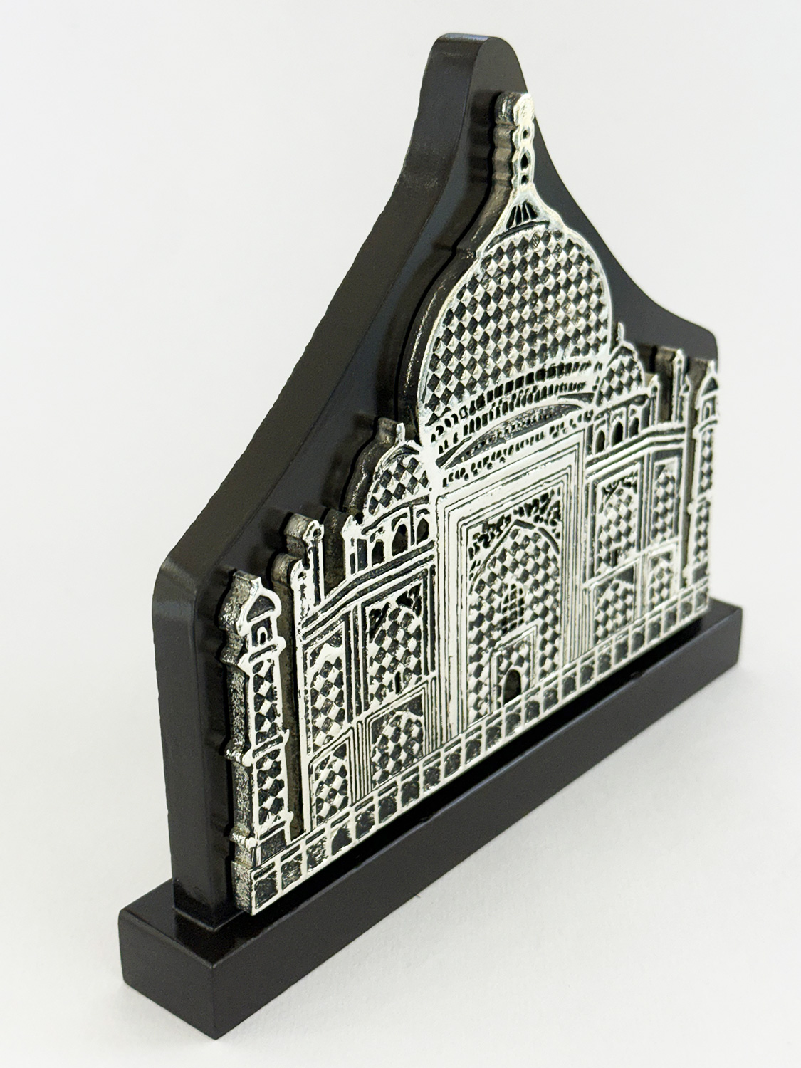 Decorative black plaque in the shape of a Taj Mahal-inspired facade with intricate white engravings on a black stand