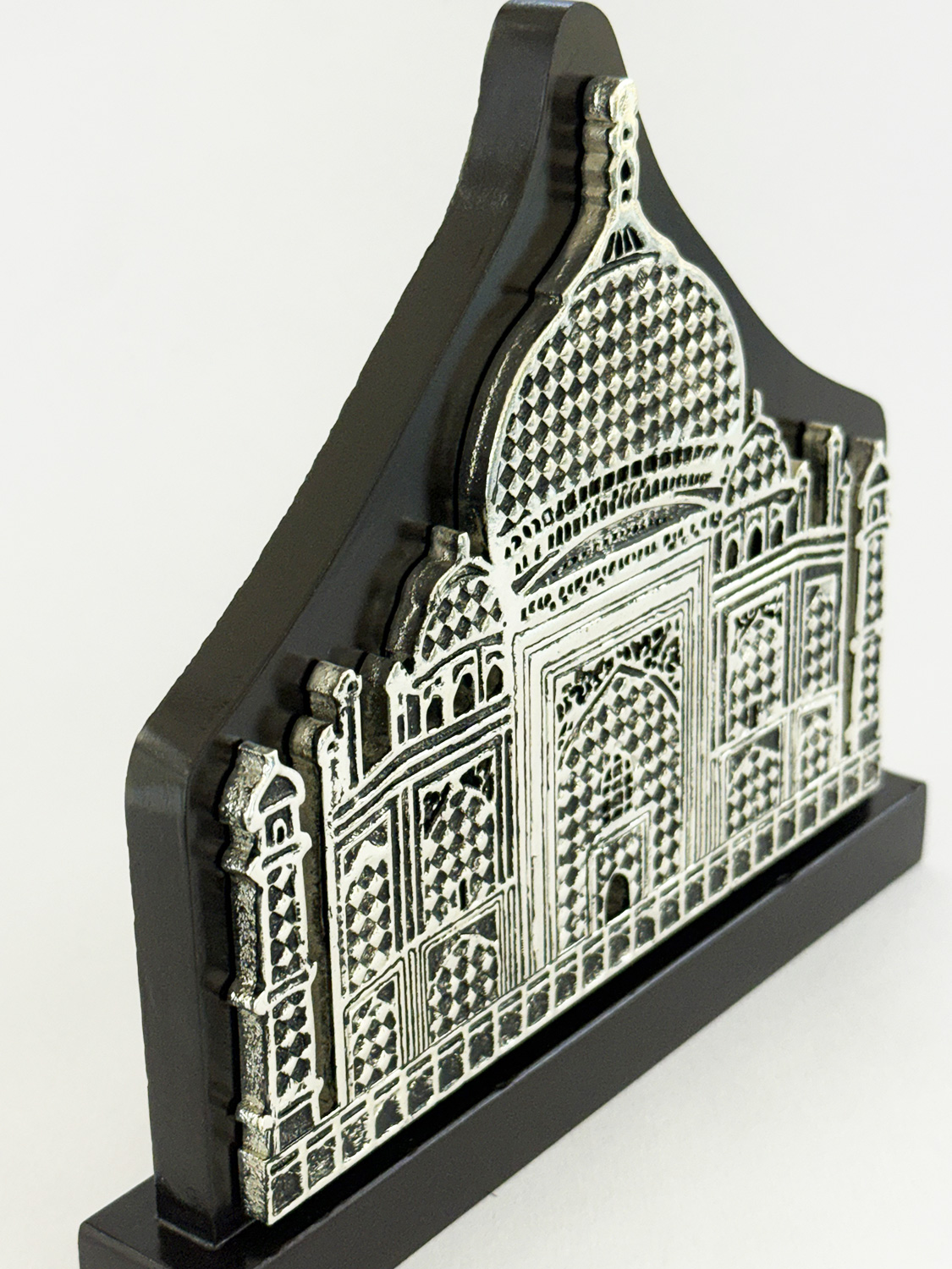 Silver-toned decorative relief of the Taj Mahal, mounted on a black display stand, showcasing intricate lattice and arches.