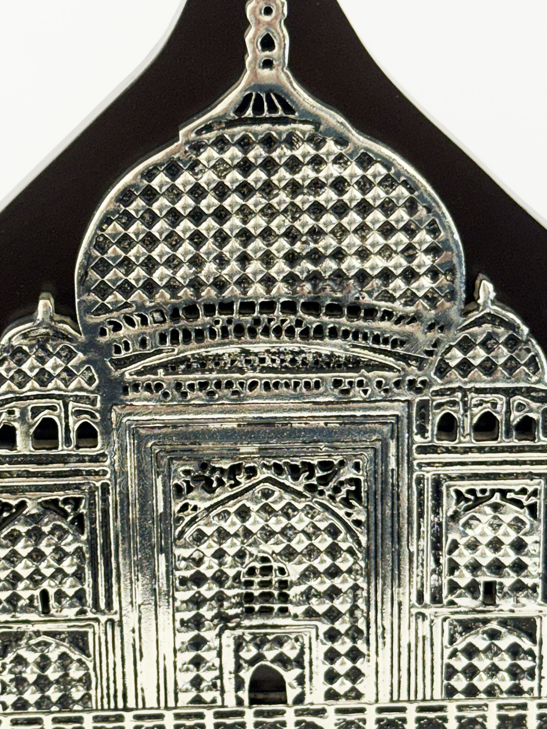 Close-up of a silver ornate metal architectural ornament with a domed crown and diamond-pattern latticework, resembling a decorative gate element.