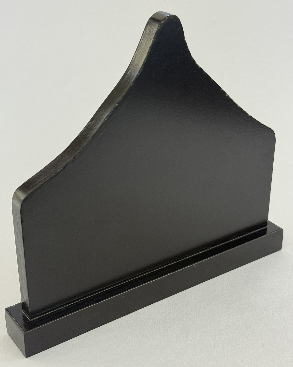 Black wooden bookend with a curved, decorative top and rectangular base, standing on a light surface.