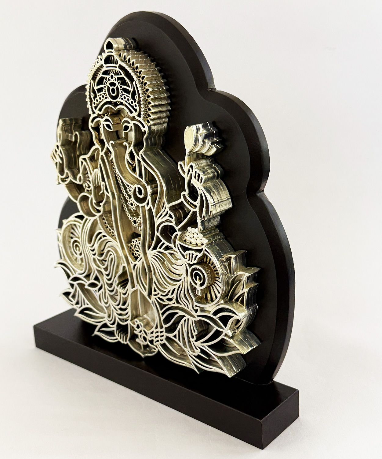 Intricately cut metal sculpture of Ganesha with ornate headdress, mounted on a black base.