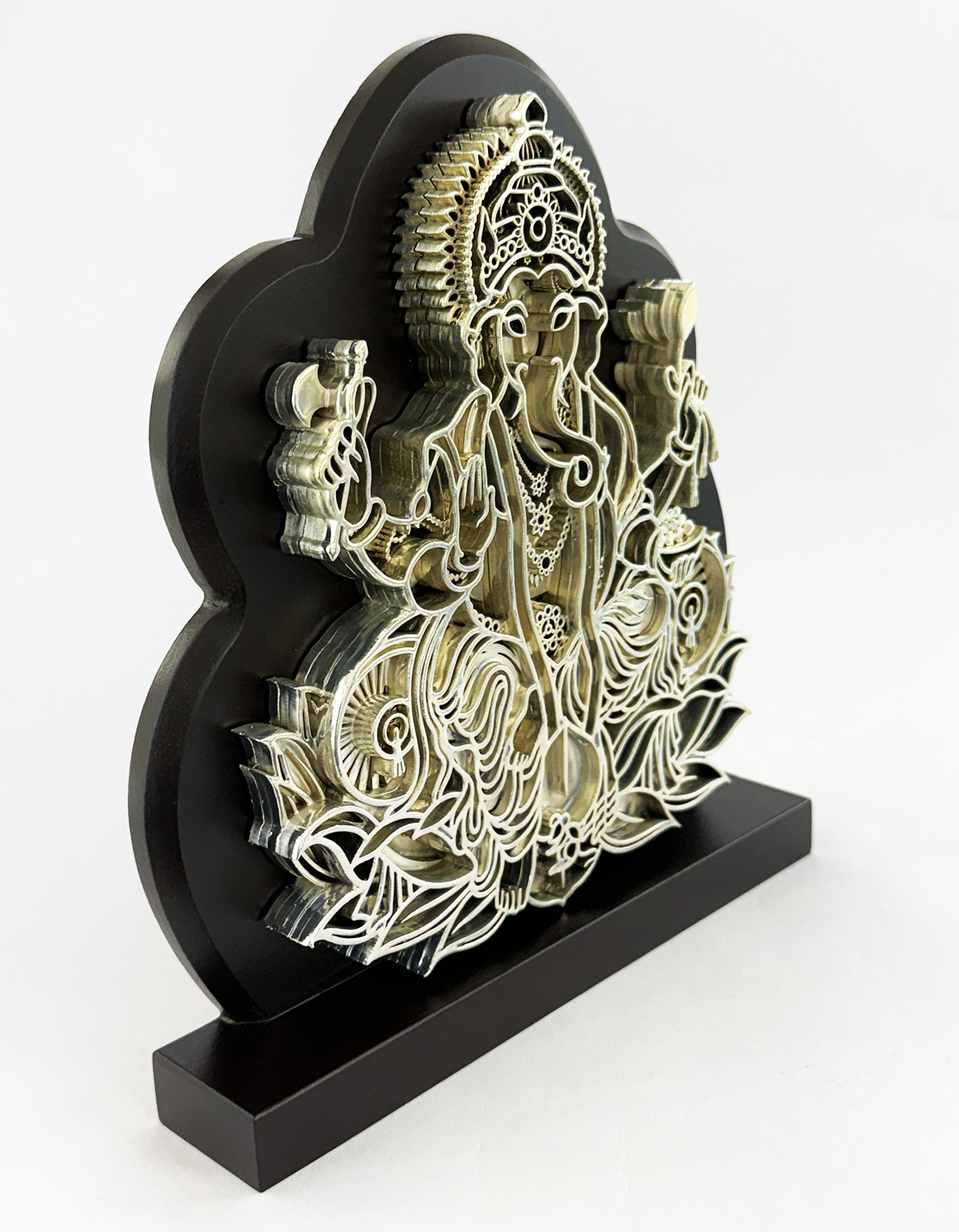 Intricately layered metal sculpture of a multi-armed deity perched among flowers on a black cloud-shaped stand.