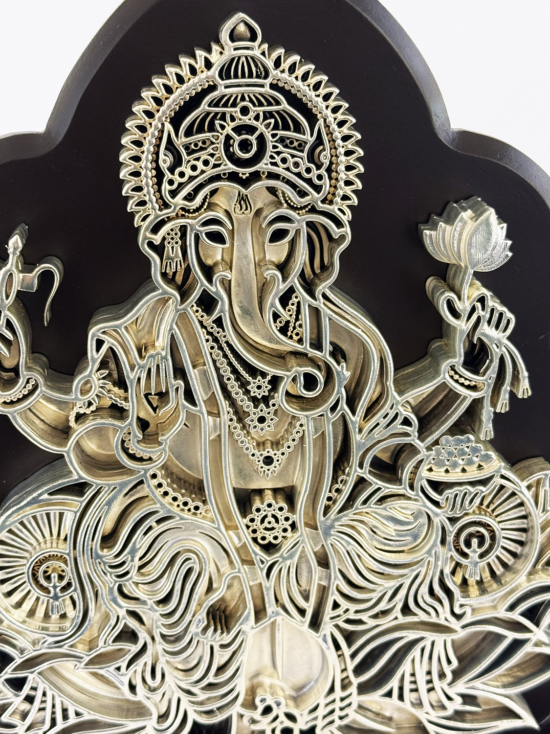 Intricate metal relief of the Hindu god Ganesha with a crown, multiple arms, and decorative jewelry on a dark background.