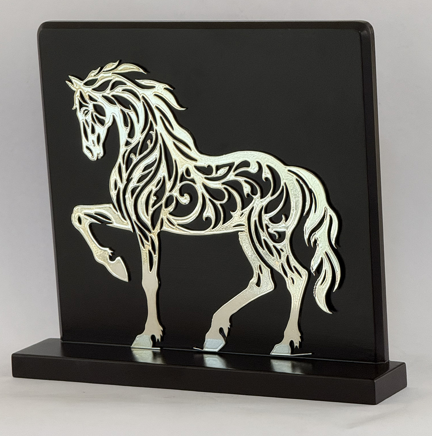 Decorative metal horse silhouette cutout mounted on a black plaque with a base plate.