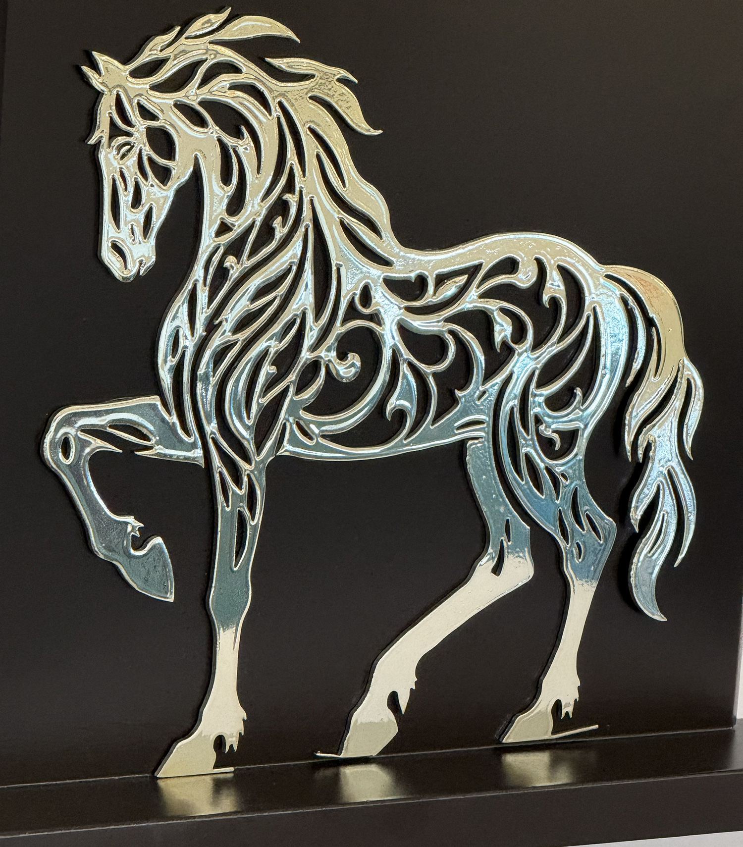 Silver metal cutout of a prancing horse with swirling, decorative patterns on a dark wall.