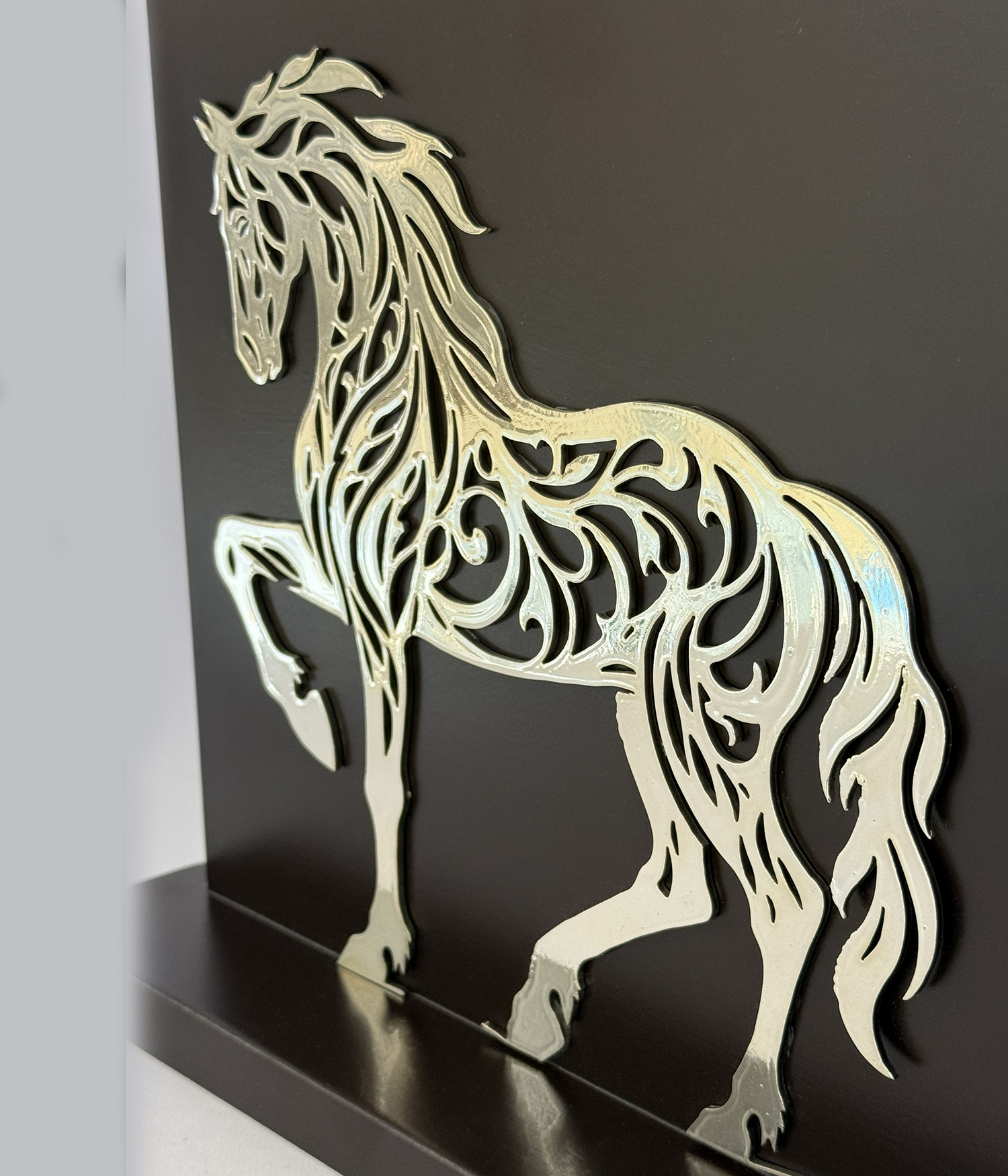 Metallic horse silhouette with an intricate cutout design mounted on a dark panel/shelf surface