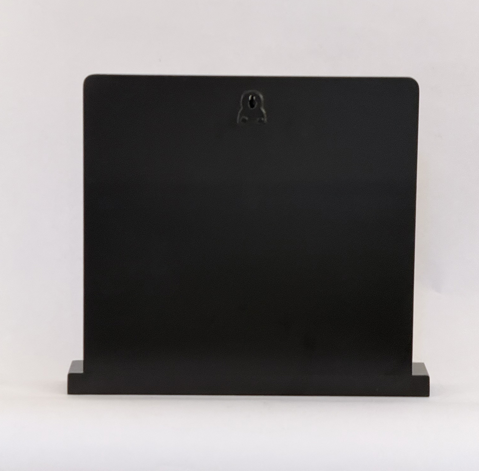 Back view of a black rectangular panel or monitor on a short base, with a small circular keyhole near the top center.