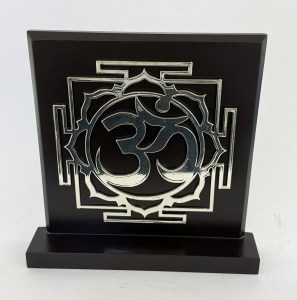Black plaque with an ornate raised silver emblem featuring a circular, swirling design inside a square frame, mounted on a base.
