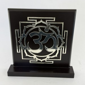 Black plaque with an ornate raised silver emblem featuring a circular, swirling design inside a square frame, mounted on a base.