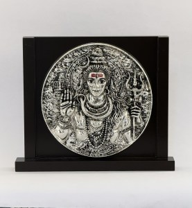 Silver-toned circular relief of Shiva as Nataraja with multiple arms and ornate halo, mounted on a black display stand.