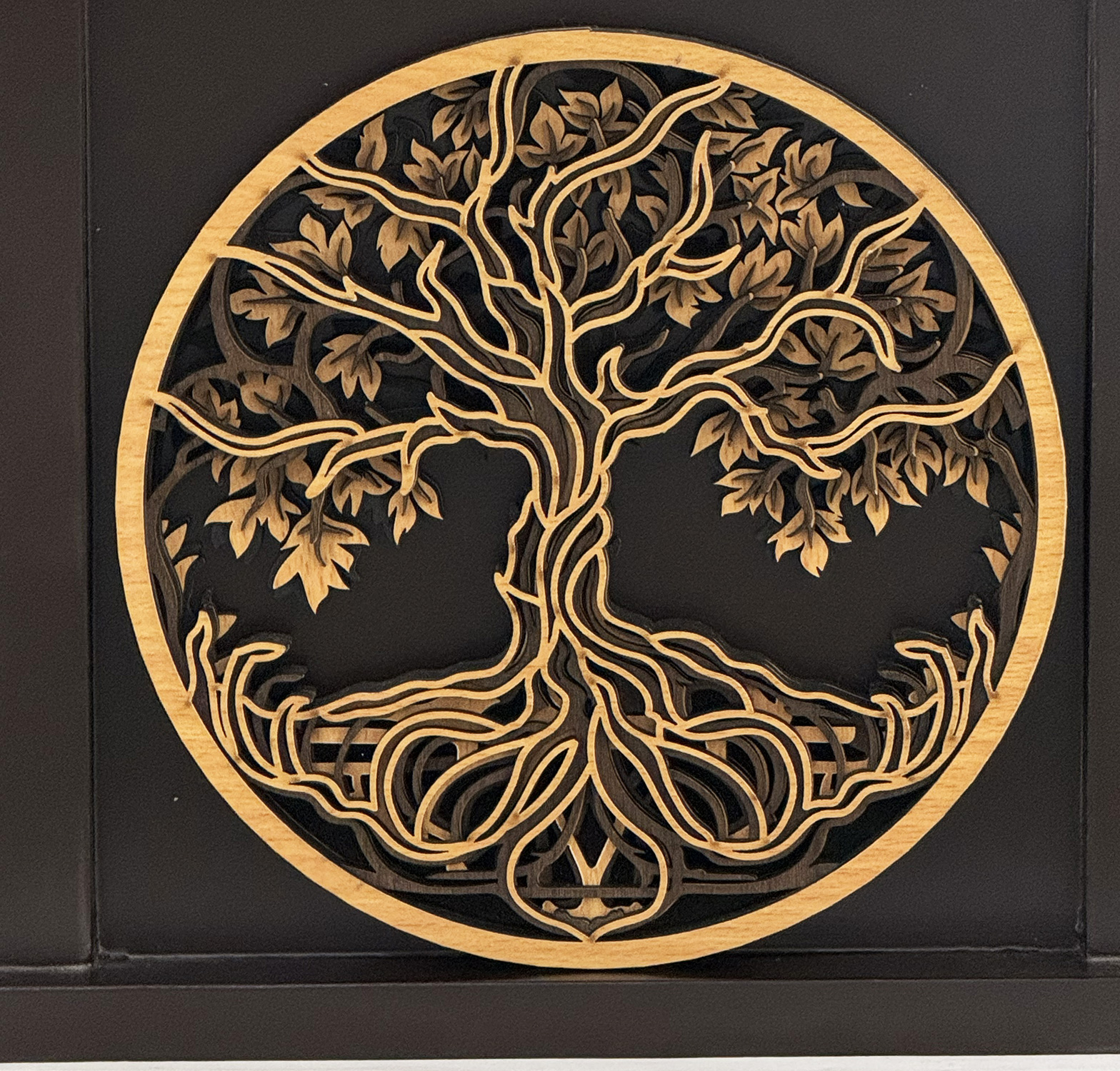 Decorative round wooden tree-of-life carving in a gold circle on a dark wall background, intricate branches and leaves extending outward.