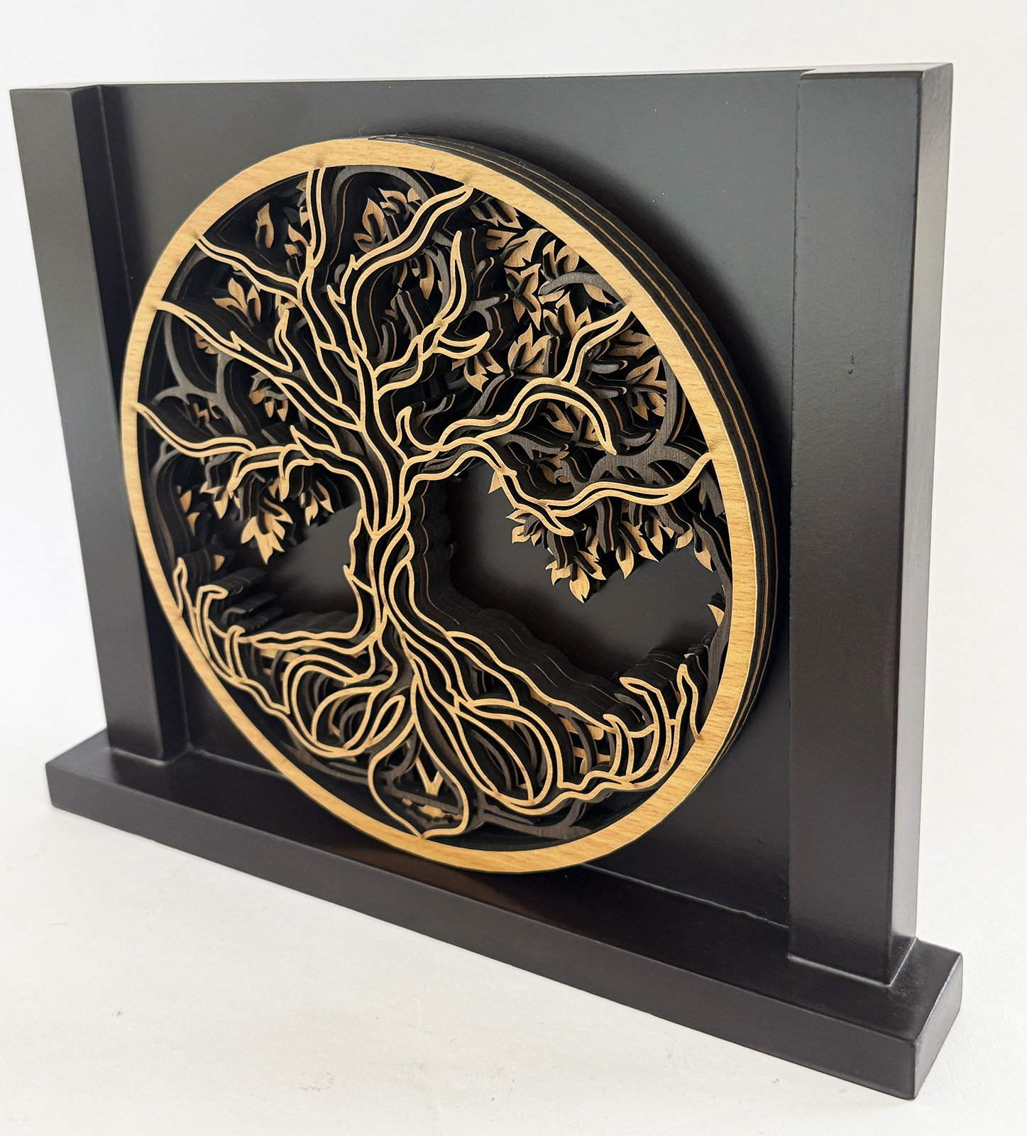 Wooden, layered tree relief in a circular frame mounted on a black rectangular display pedestal.