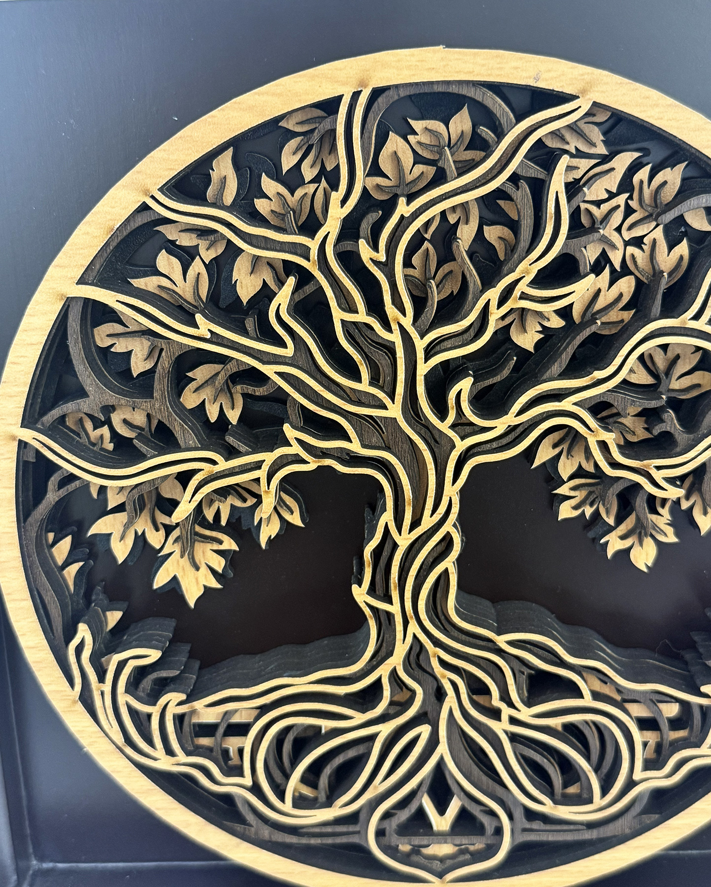 Intricate wooden tree of life silhouette carved in layers inside a circular frame, with twisting branches and leaves against a dark background, decorative artwork