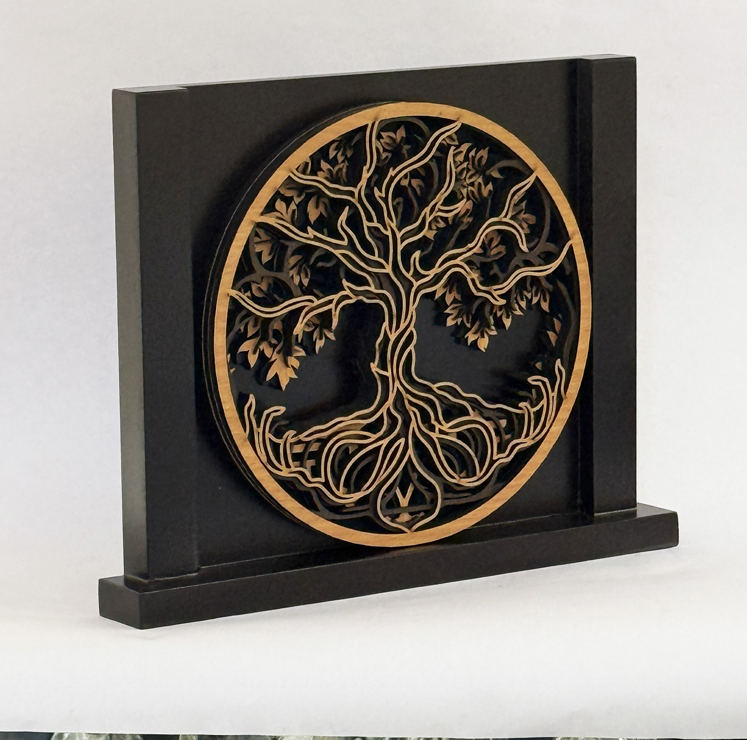 Decorative black wooden plaque with a gold circular tree-of-life design on a rectangular stand.