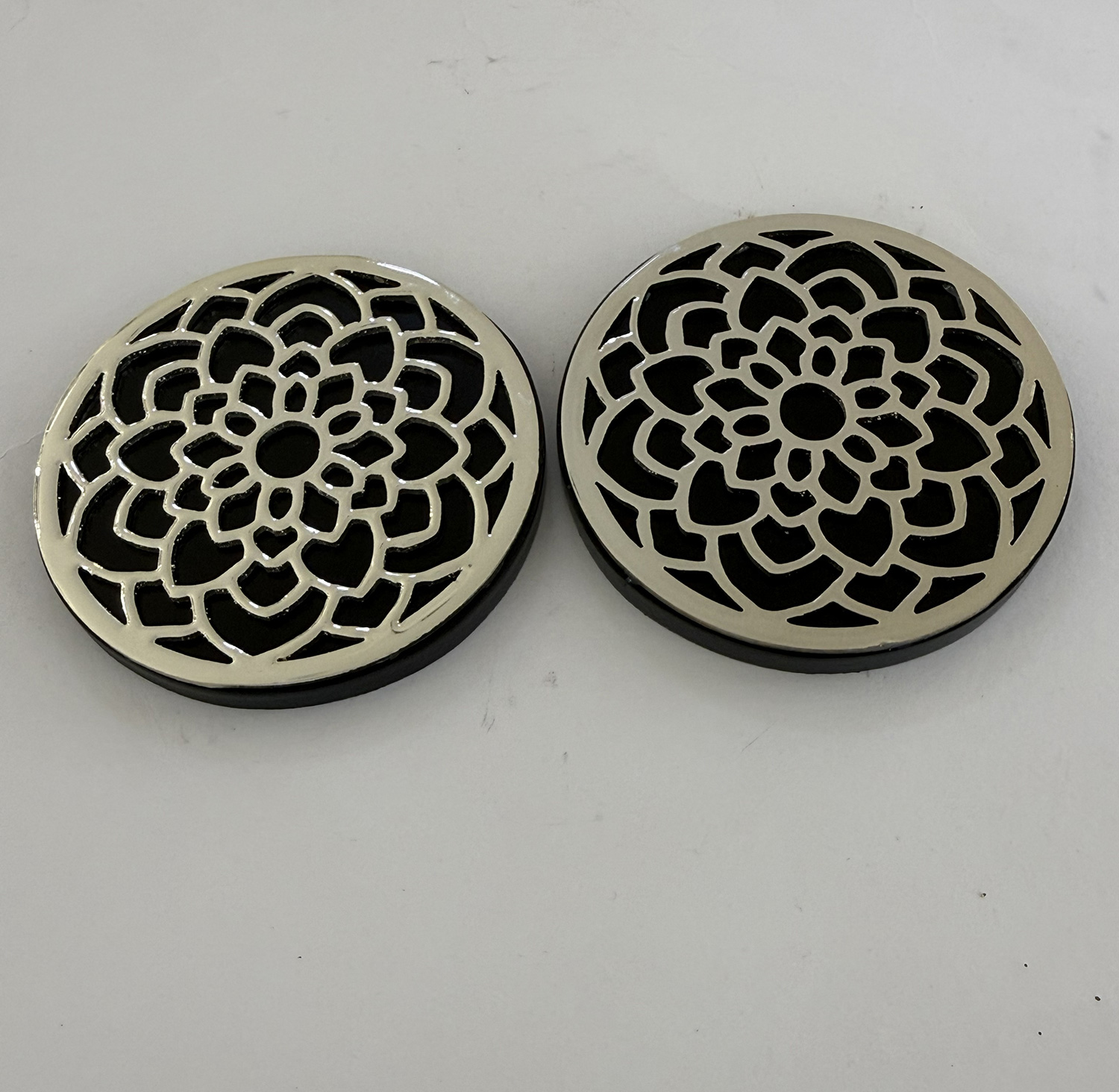 Two round metal coasters with intricate floral lattice cutouts on a dark background, placed side by side.