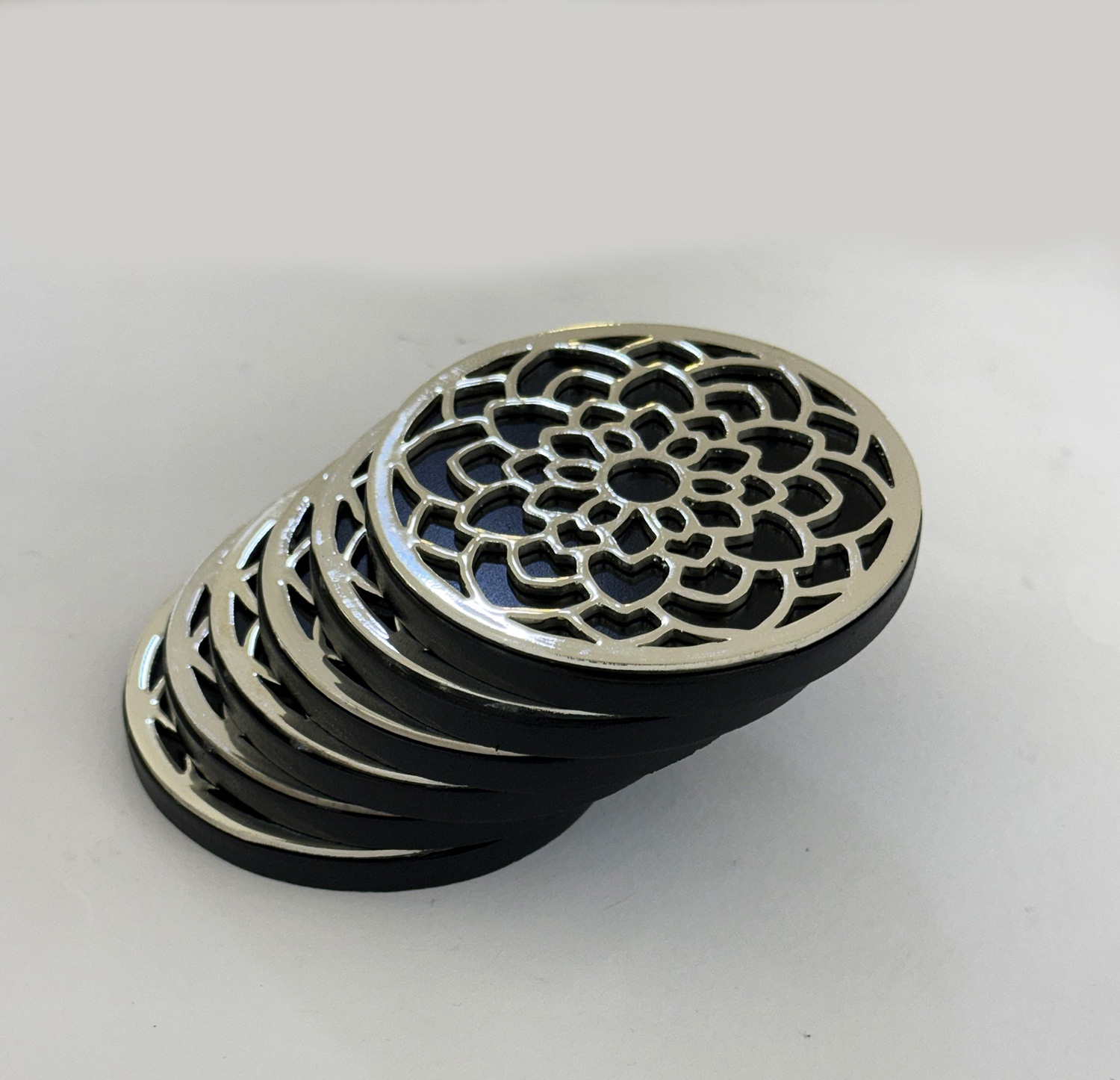 Stacked round metal drain covers with an intricate floral lattice pattern on a light surface