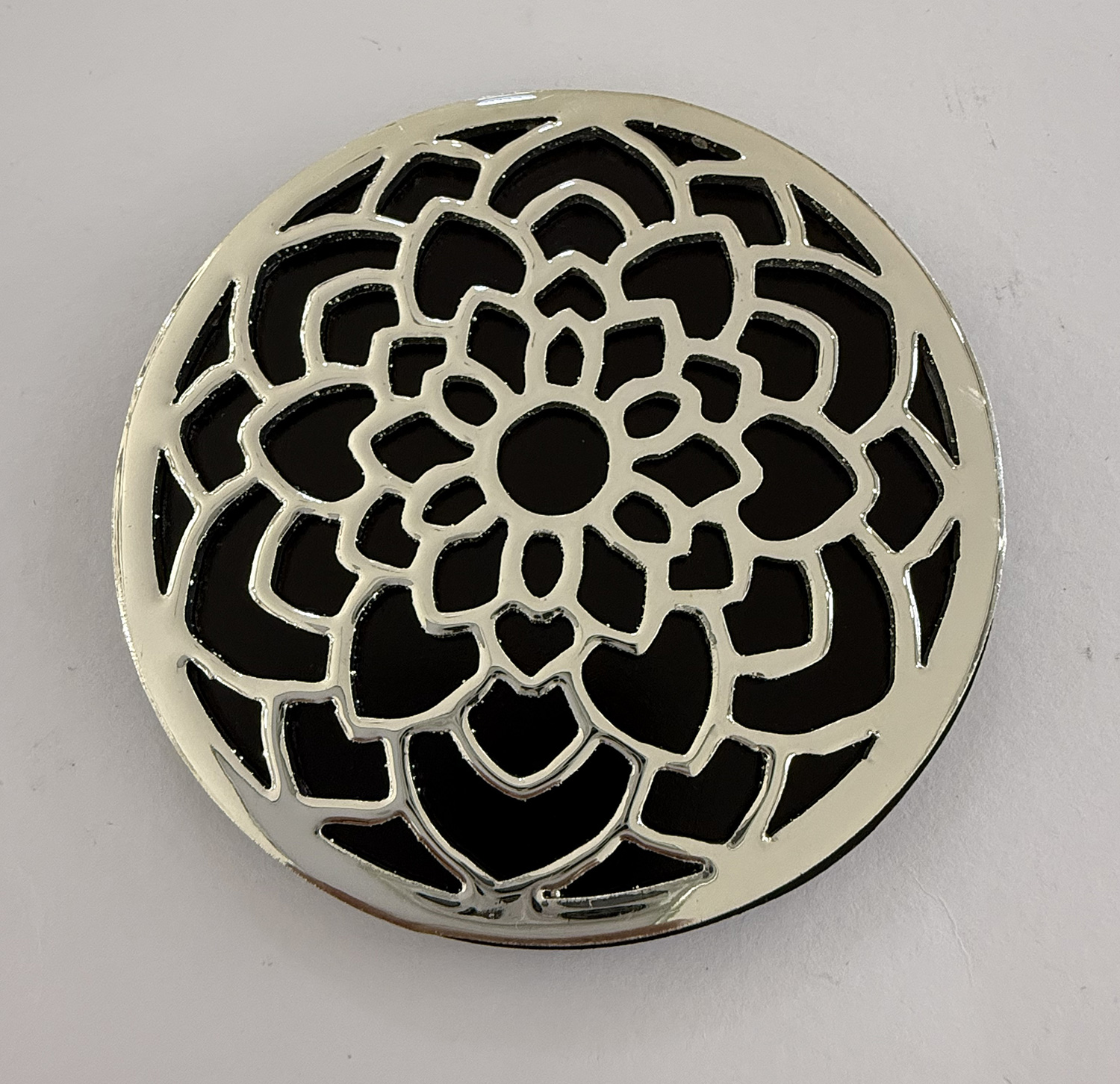 Round metal grate with a floral lattice pattern in silver against a black background.