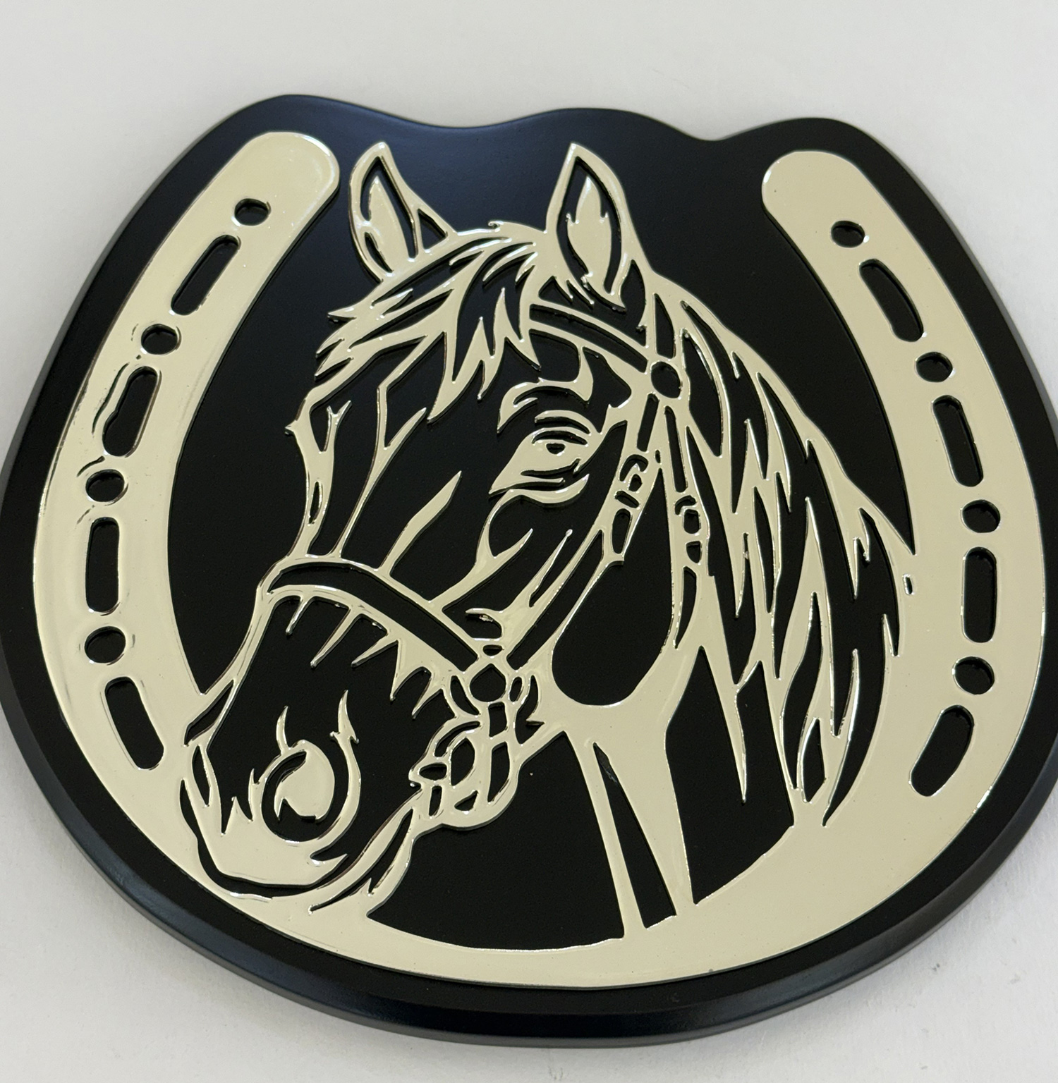 Circular plaque featuring a cream horse head silhouette within a beige horseshoe frame on a black background.