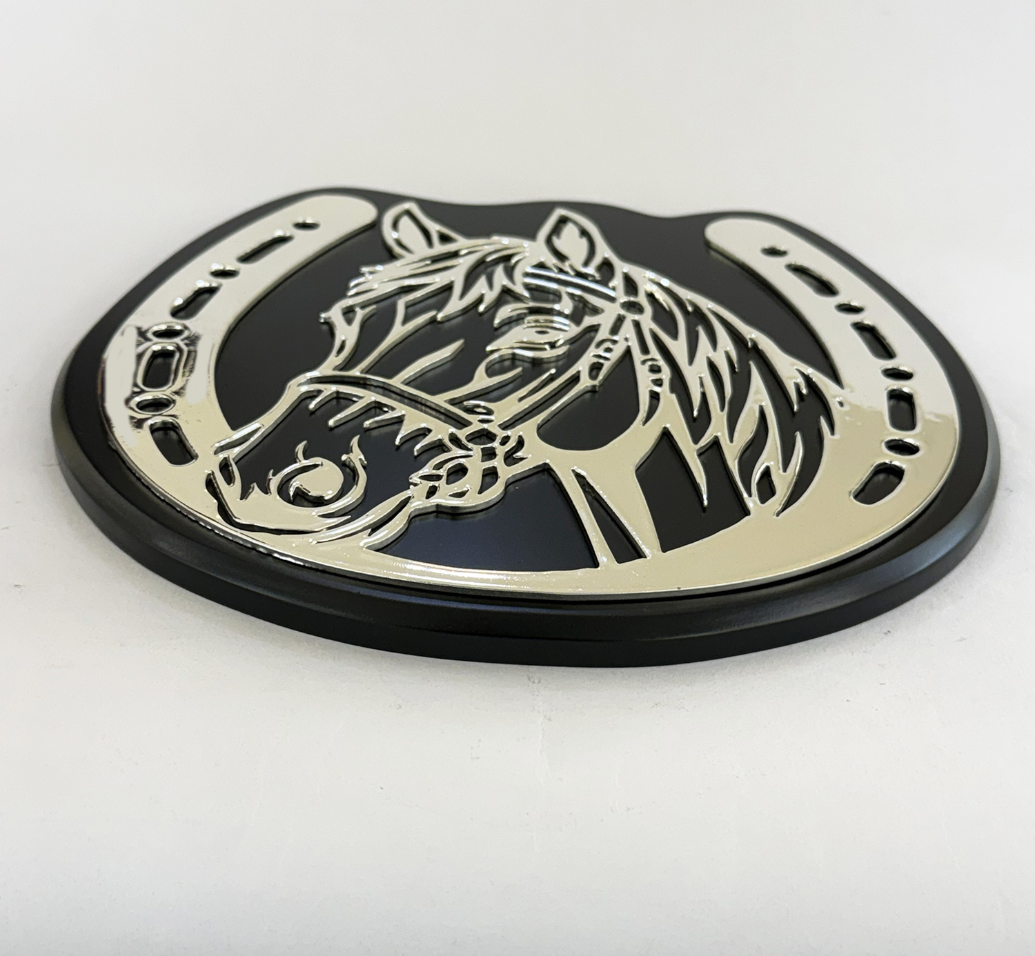 Shiny silver horse head silhouette cut from metal mounted on a dark oval base, a decorative emblem or plaque