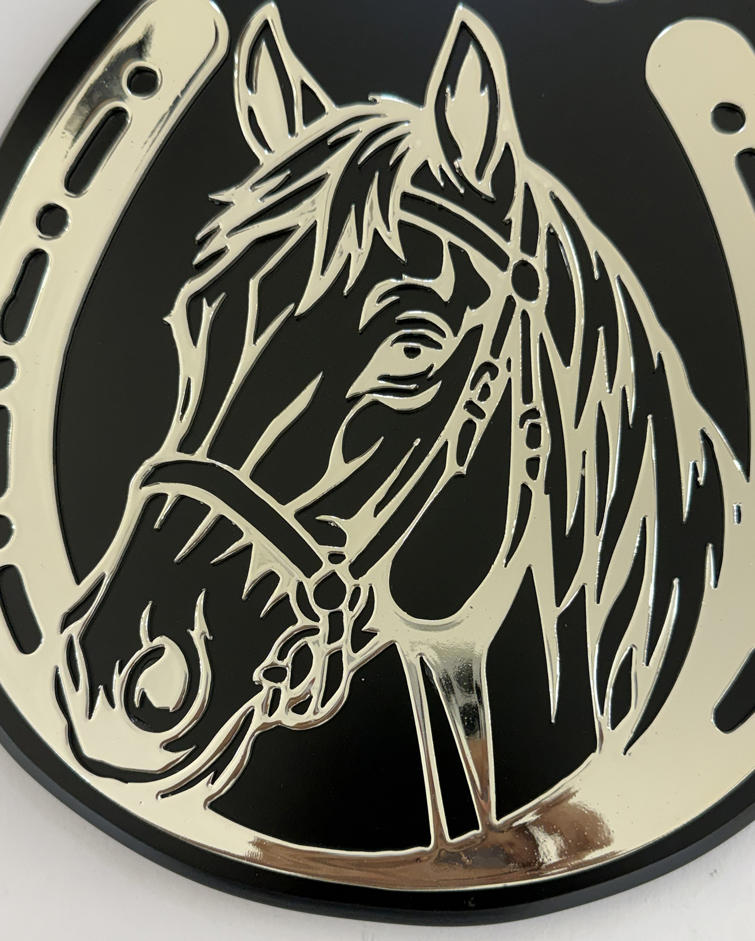 Close-up of a silver embossed horse head logo on a black circular badge with perforated edge bands nearby.