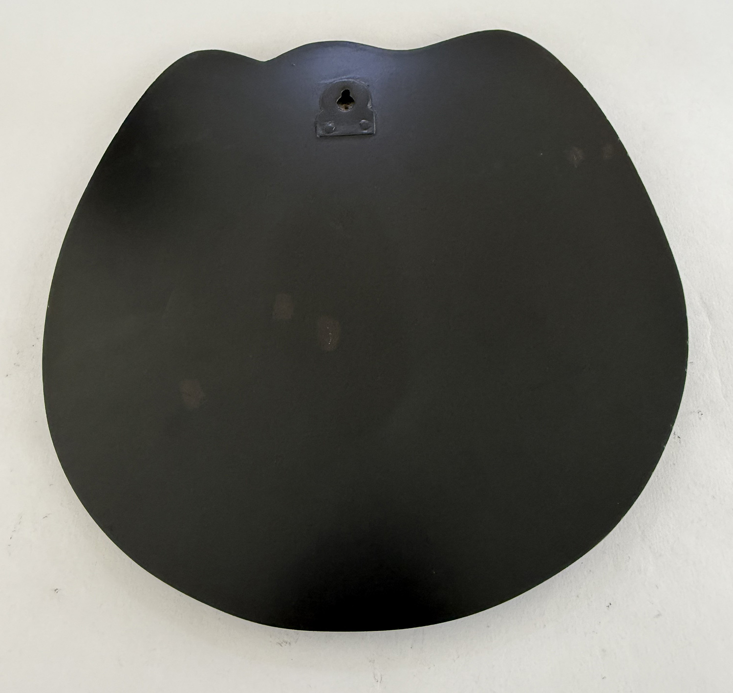 Large irregular black circular plate with a small metal mounting plate and central hole near the top edge.