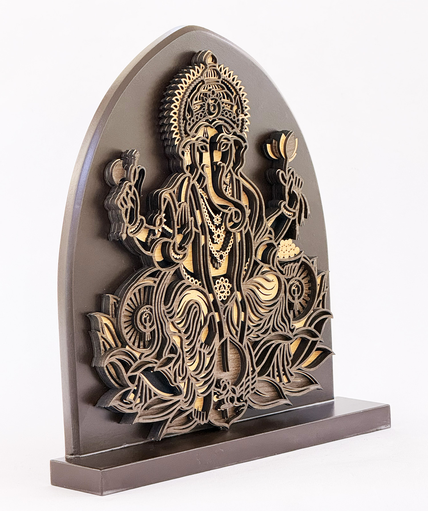 Intricately cut wooden sculpture of a seated Hindu goddess with multiple arms, mounted on a dark arch-shaped plaque.