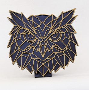 Abstract owl sculpture built from blue polygonal panels with tan edges, mounted on a square base on a white background.