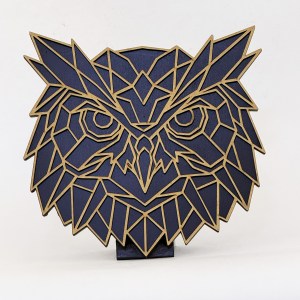 Abstract owl sculpture built from blue polygonal panels with tan edges, mounted on a square base on a white background.