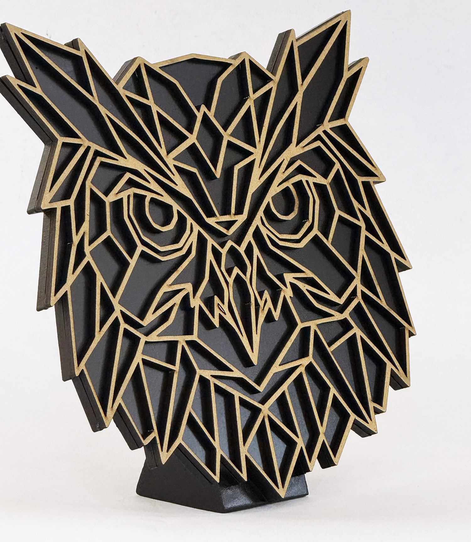 Abstract geometric sculpture of an owl's head formed by tan-edged panels on a black base, against a light background.