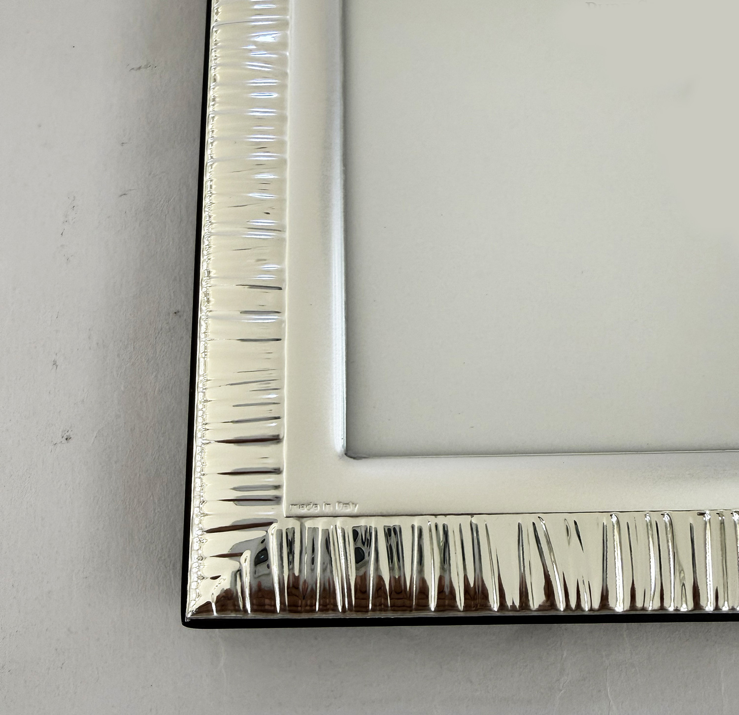 Close-up of a silver ribbed metal picture frame corner with 'made in Italy' inscription visible.