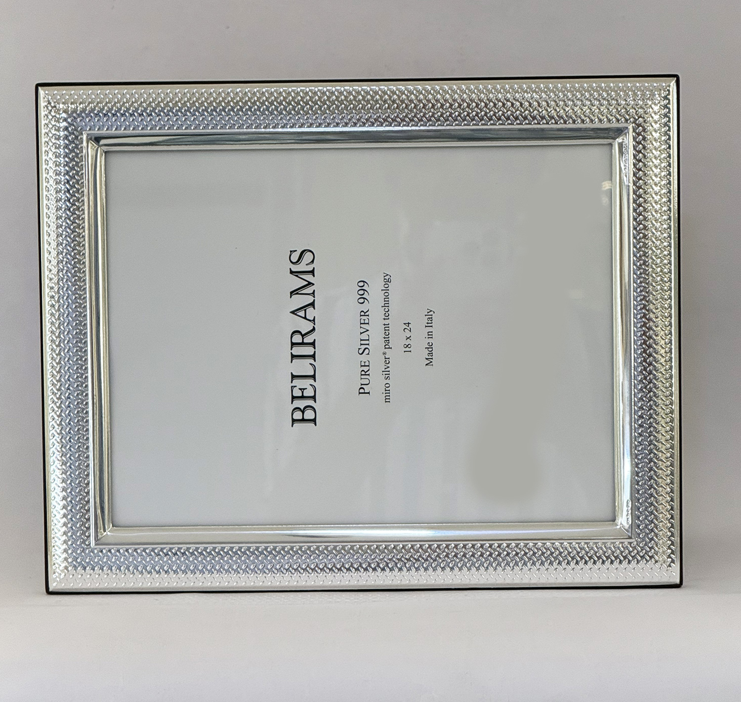 Silver textured picture frame with a white label inside showing product text like 'PURE SILVER 999' and 'Made in Italy'