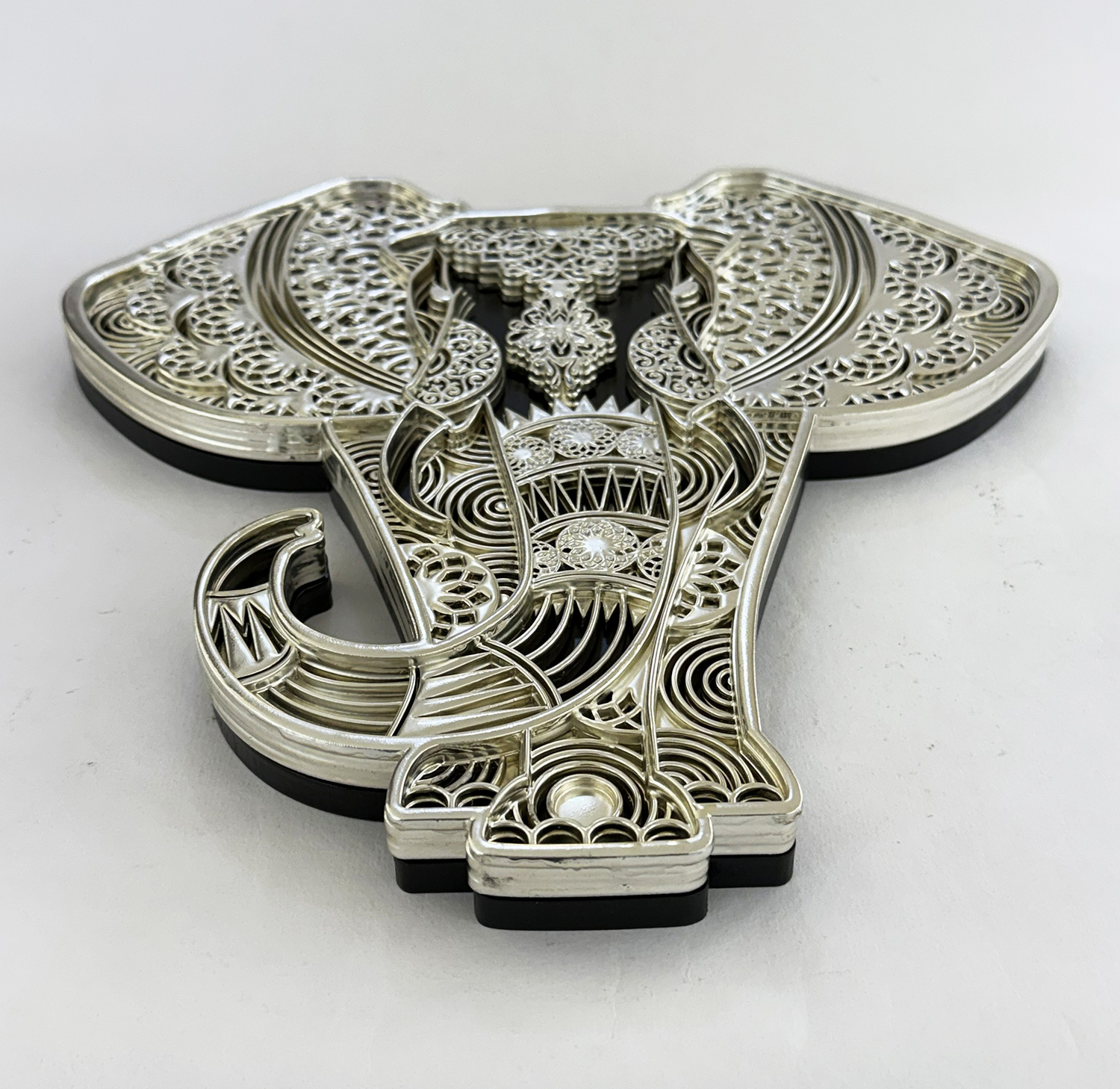 Intricately cut silver filigree metal sculpture with layered, lace-like patterns.