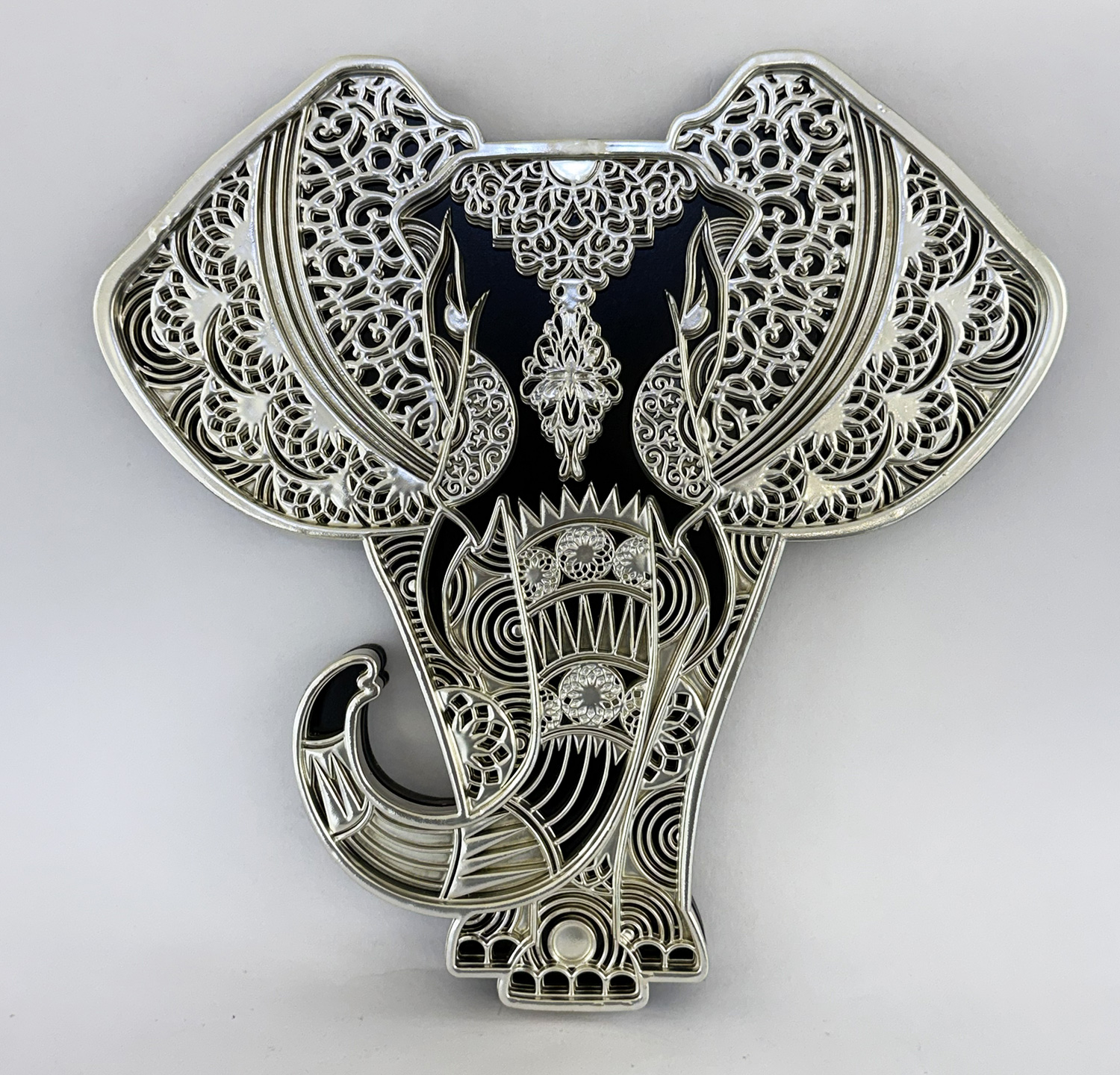 Ornate silver elephant pendant with intricate lace-like filigree and black enamel background.