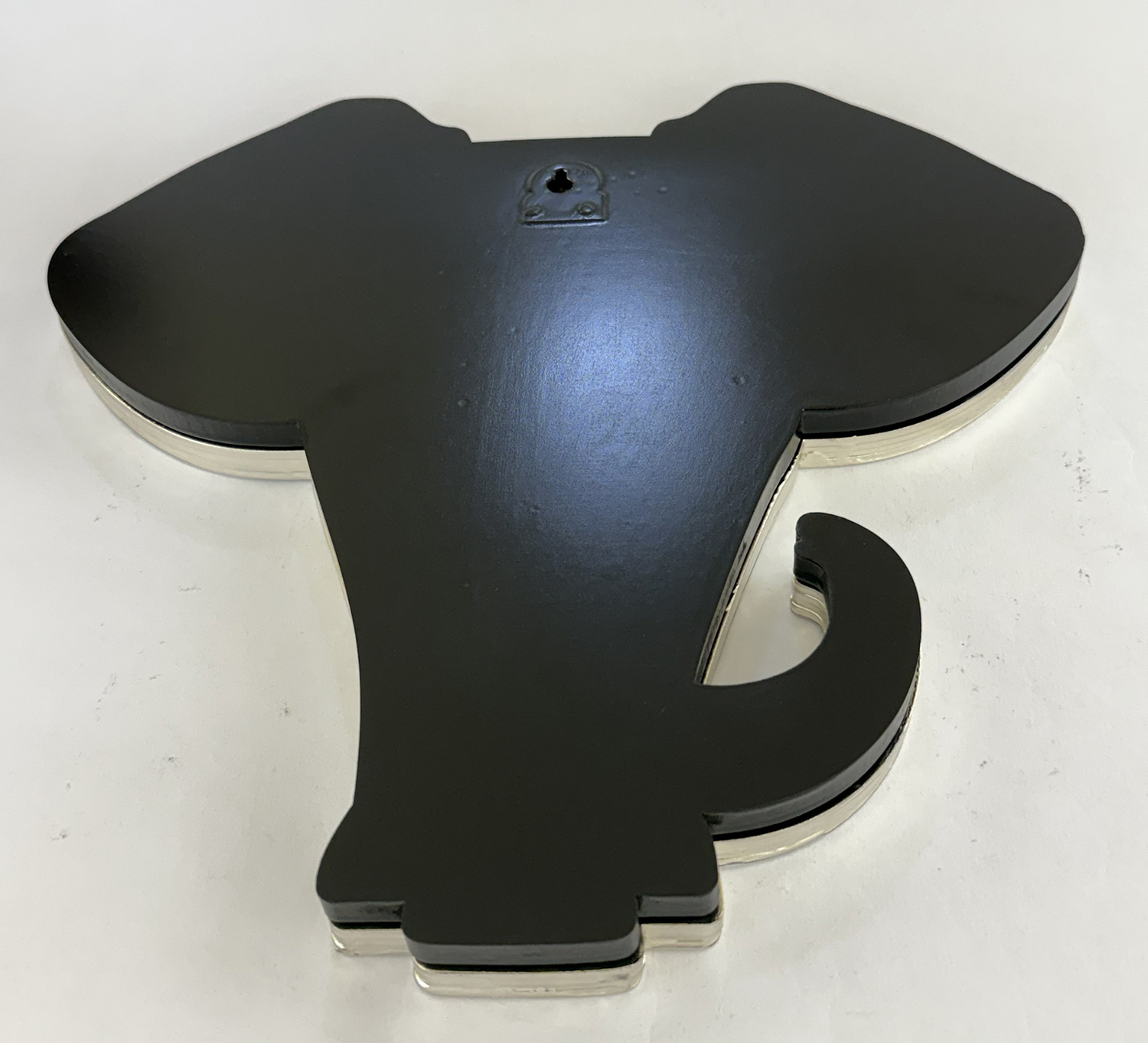 Close-up of a black irregularly shaped plastic object with curved arms and a visible screw on top, resting on a white surface.