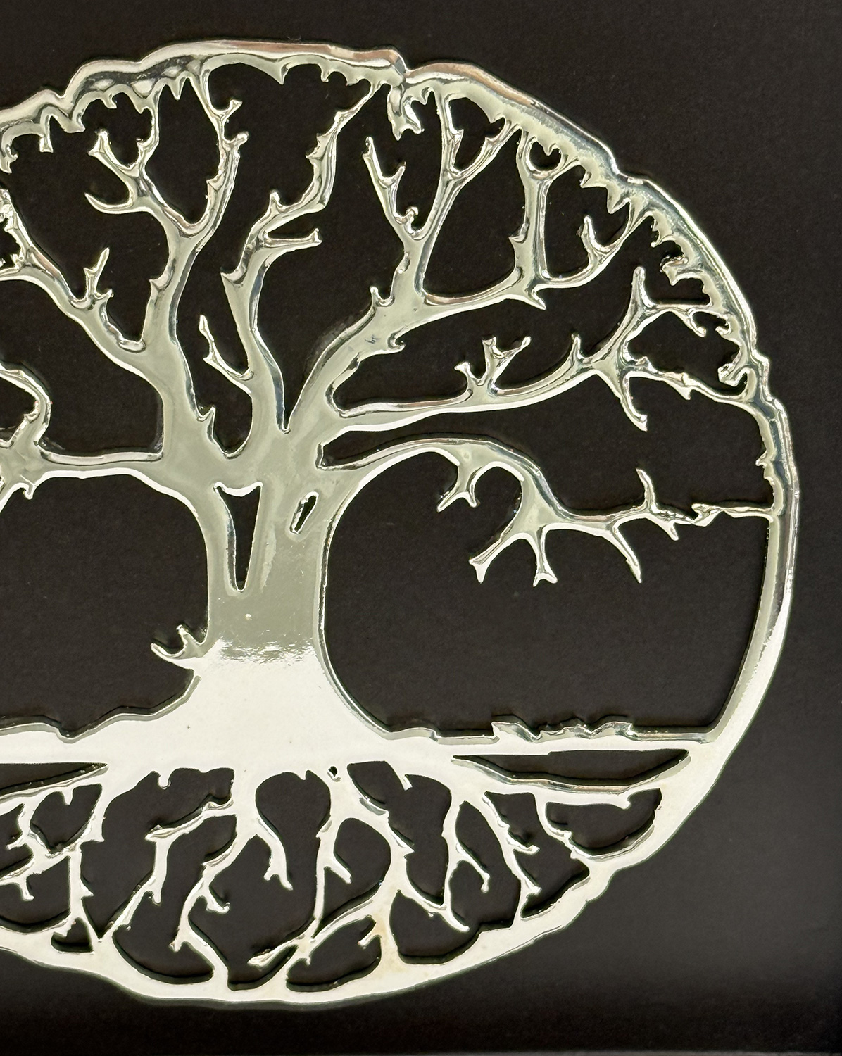 Silvery tree silhouette with intricate branches forming a circular shape on a dark background.